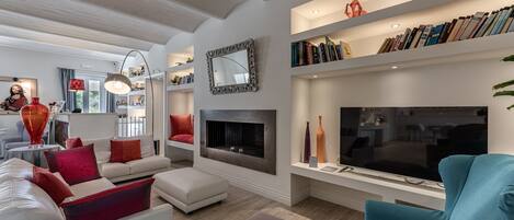 A modern living room with a fireplace, white sofas, a teal armchair, and a bookshelf with books.