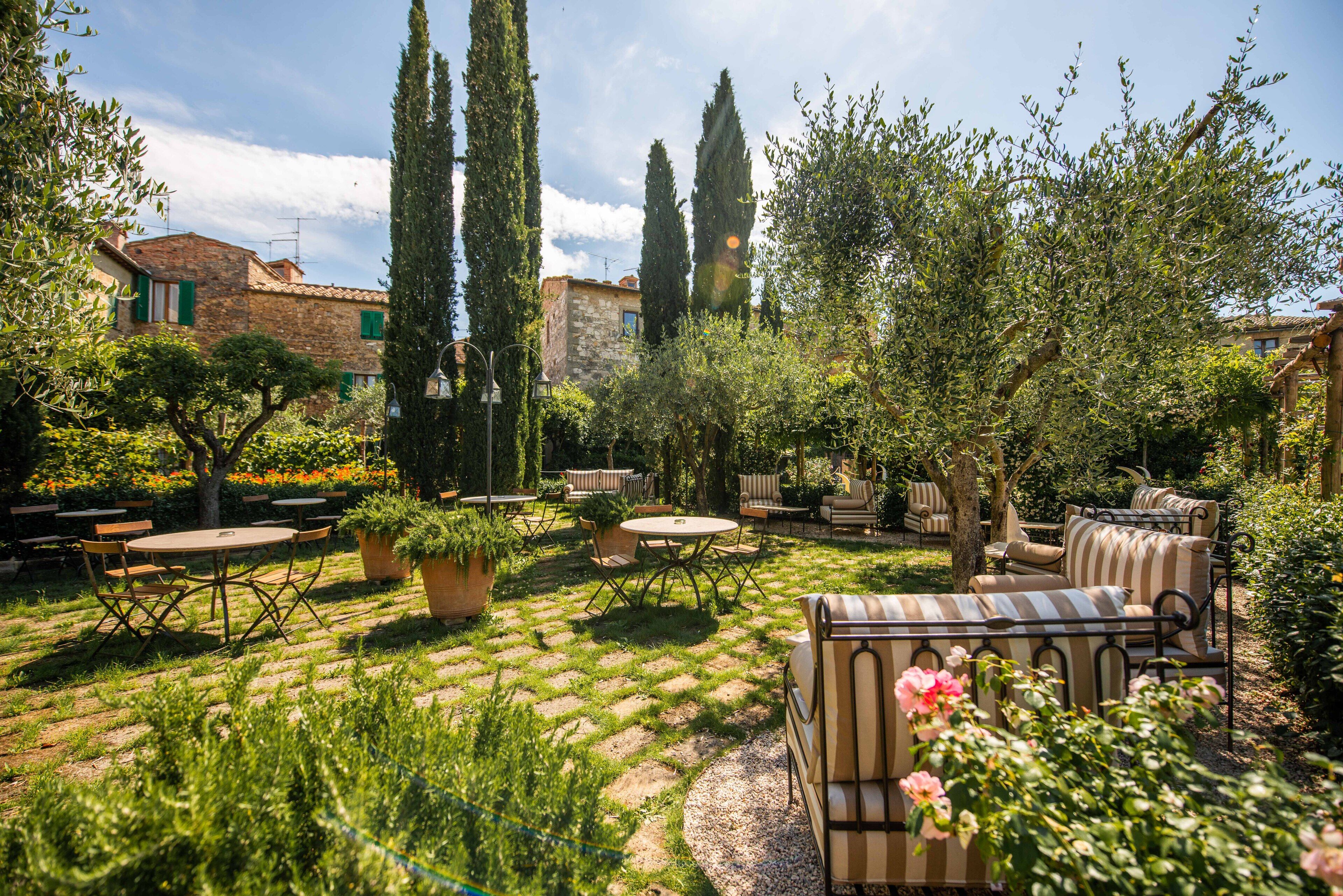 A courtyard with outdoor seating, potted plants, and tall cypress trees.