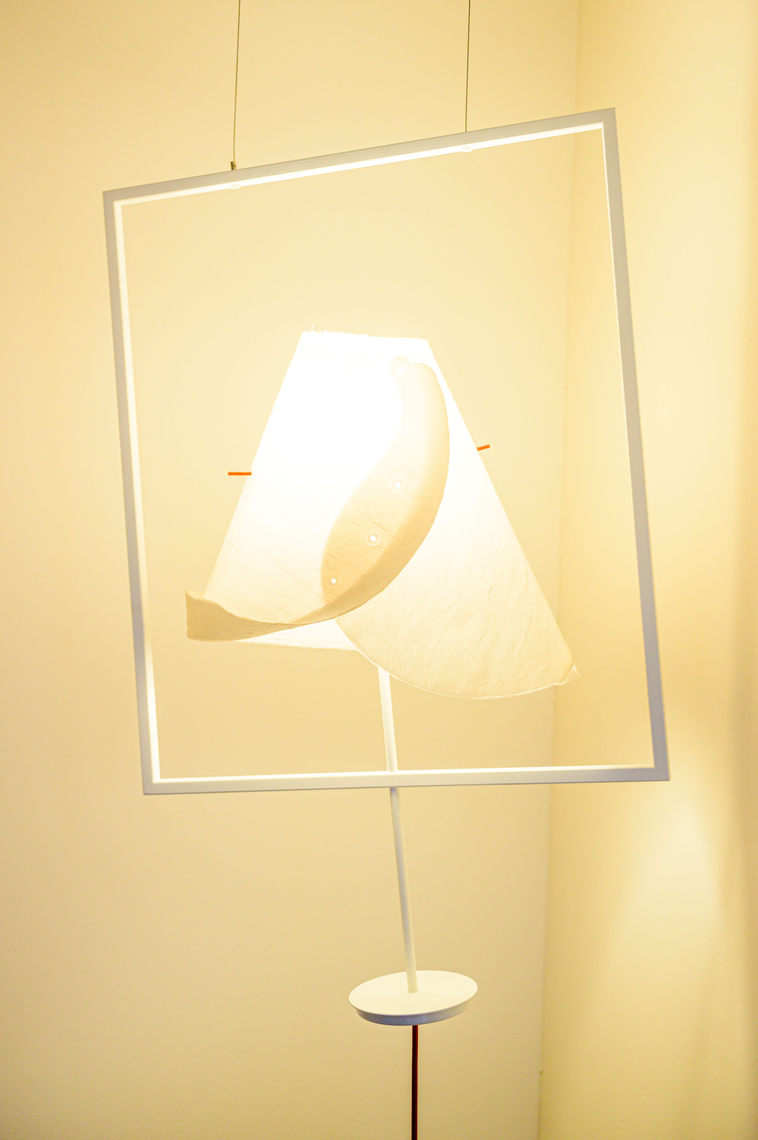 A floor lamp with a white shade and a rectangular frame against a plain wall.