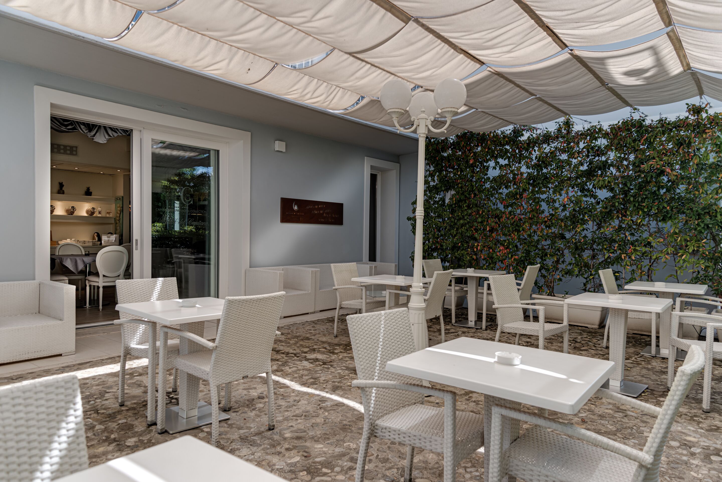 An outdoor seating area with white tables and chairs, a covered patio, and a view of a garden.