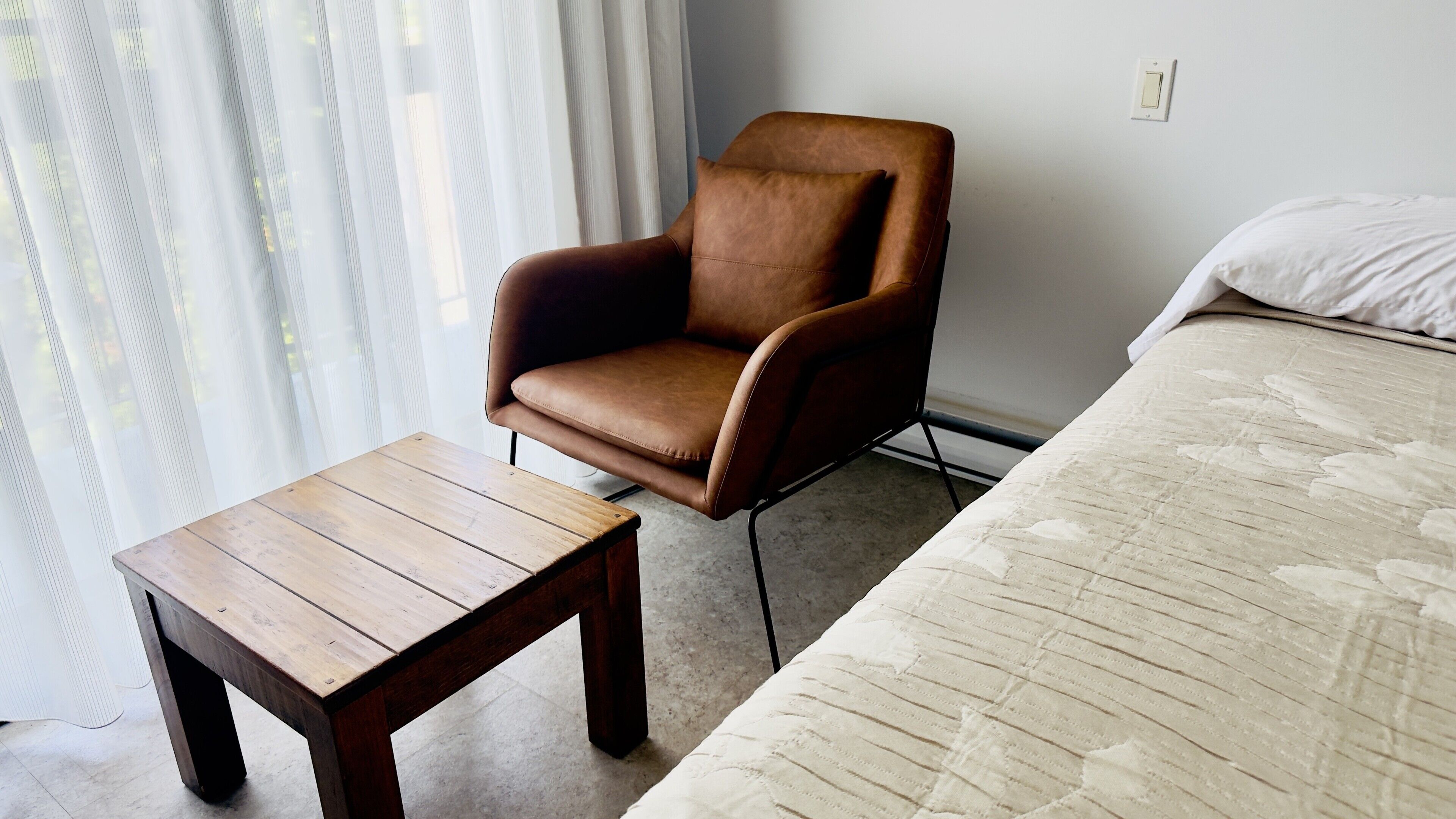 A room with a wooden table, a brown leather chair, and a bed with a quilted blanket.