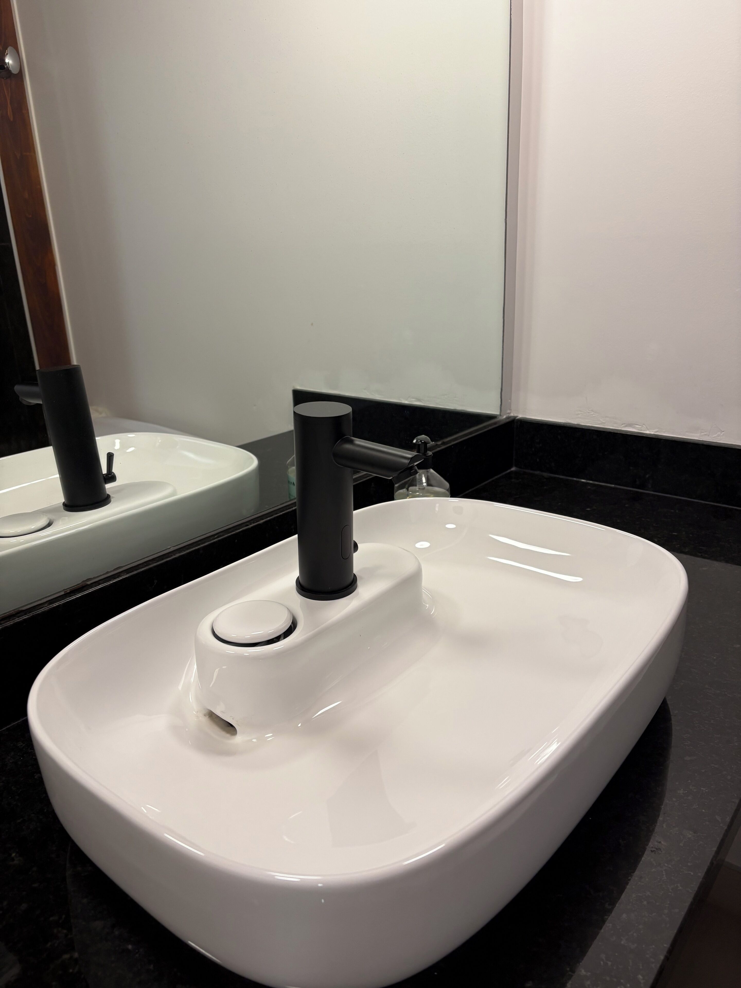 A white sink with a modern faucet, a mirror above it, and a black countertop.