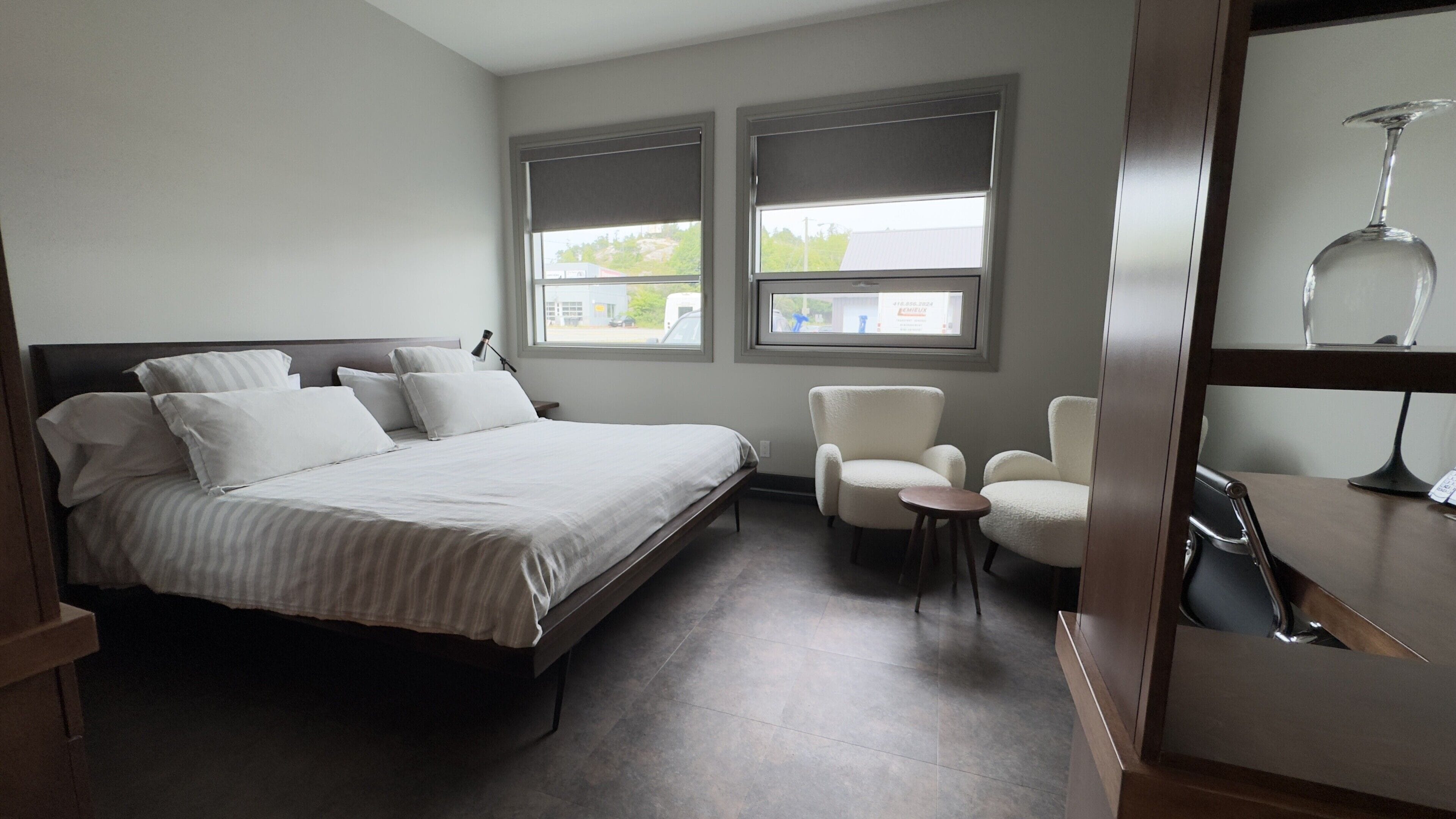 Un dormitorio con una cama, dos sillas, un escritorio y dos ventanas con persianas.