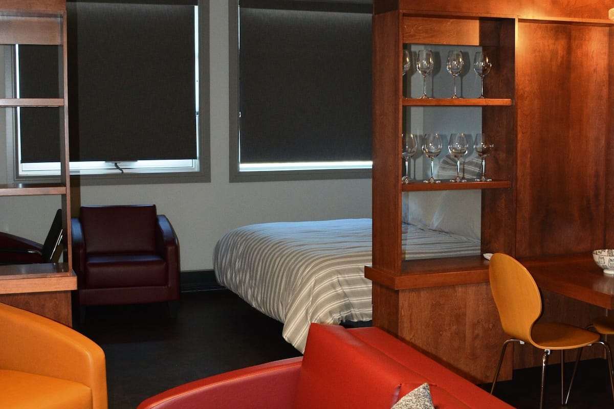 Une chambre d’hôtel moderne avec un canapé rouge, un meuble en bois contenant de la verrerie et un coin repas.