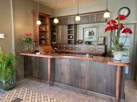 A wooden reception desk with a clock, shelves with decorative items, and potted plants.
