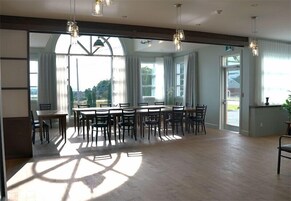 A spacious dining area with a large table and chairs, large windows with curtains, and hanging pendant lights.