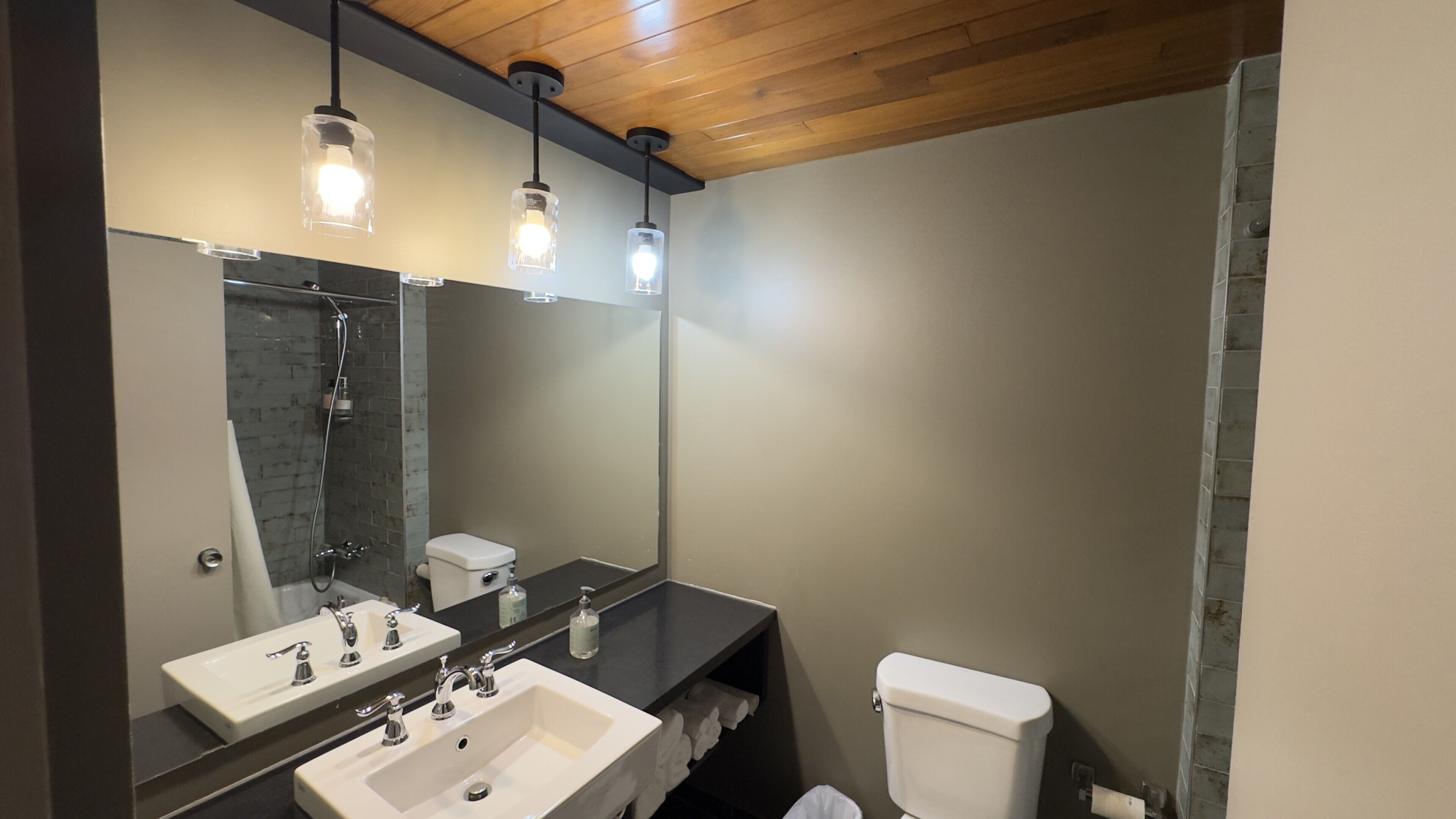 Une salle de bain avec un grand miroir, deux lavabos, des toilettes et une douche.