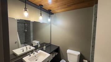 Une salle de bain avec un grand miroir, deux lavabos, des toilettes et une douche.