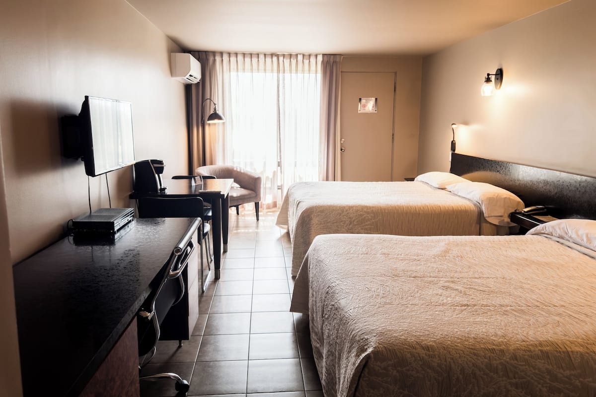 Une chambre d’hôtel avec deux lits, un bureau avec un ordinateur, un téléviseur fixé au mur et une fenêtre avec des rideaux.