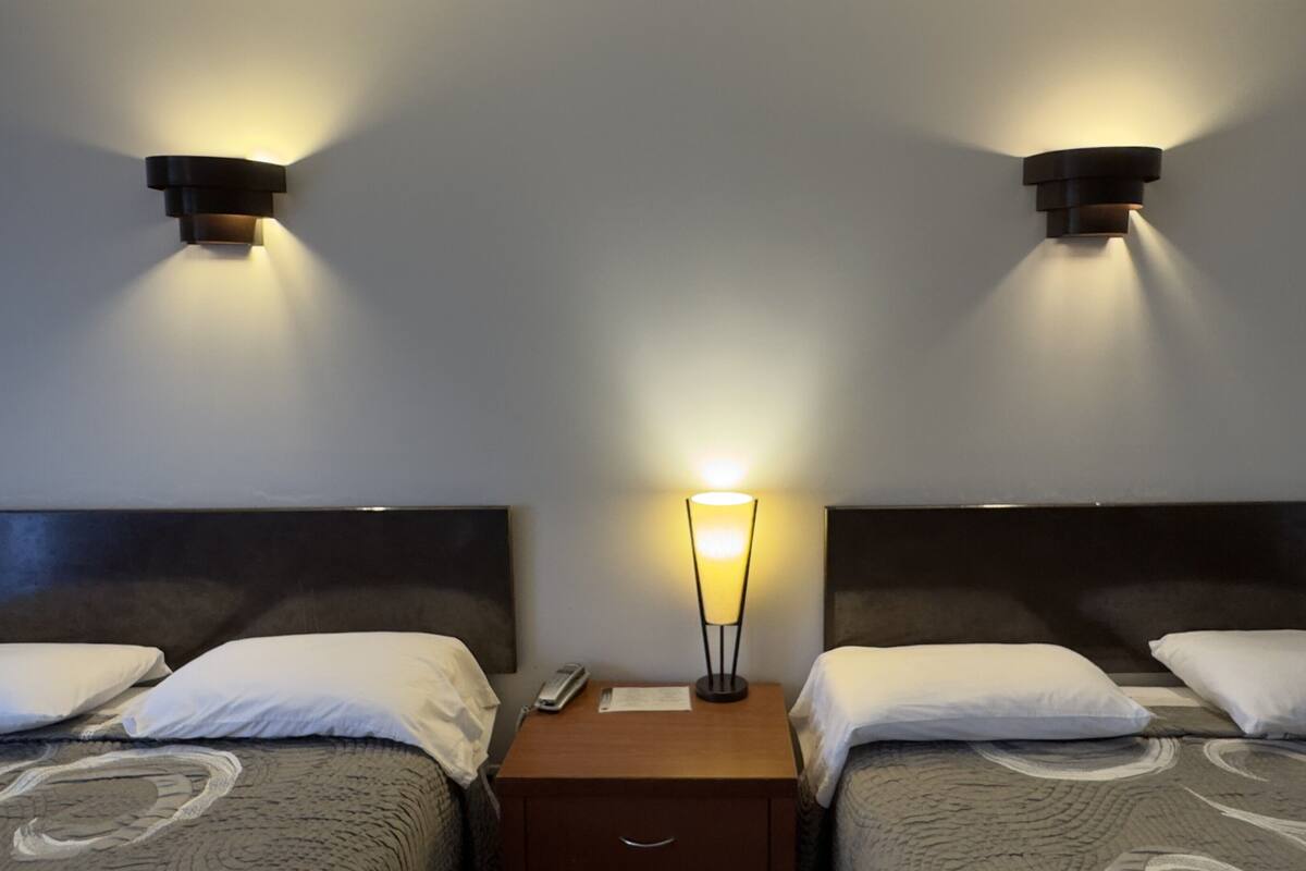 Une chambre d’hôtel avec deux lits, une table de chevet, une lampe et deux appliques murales.