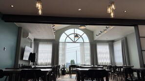 A conference room with tables and chairs, large windows with curtains, and pendant lighting. - Motel Le Martinet (La Pocatiere)