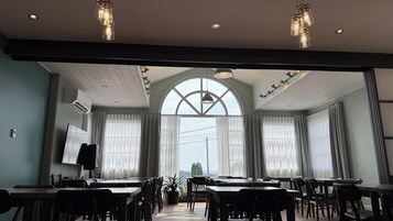 A conference room with tables and chairs, large windows with curtains, and pendant lighting.