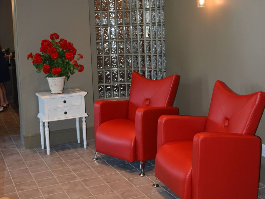 Una habitación con dos sillas rojas, una mesita auxiliar blanca con una planta en maceta, un separador de vidrio decorativo y un equipo de aire acondicionado.