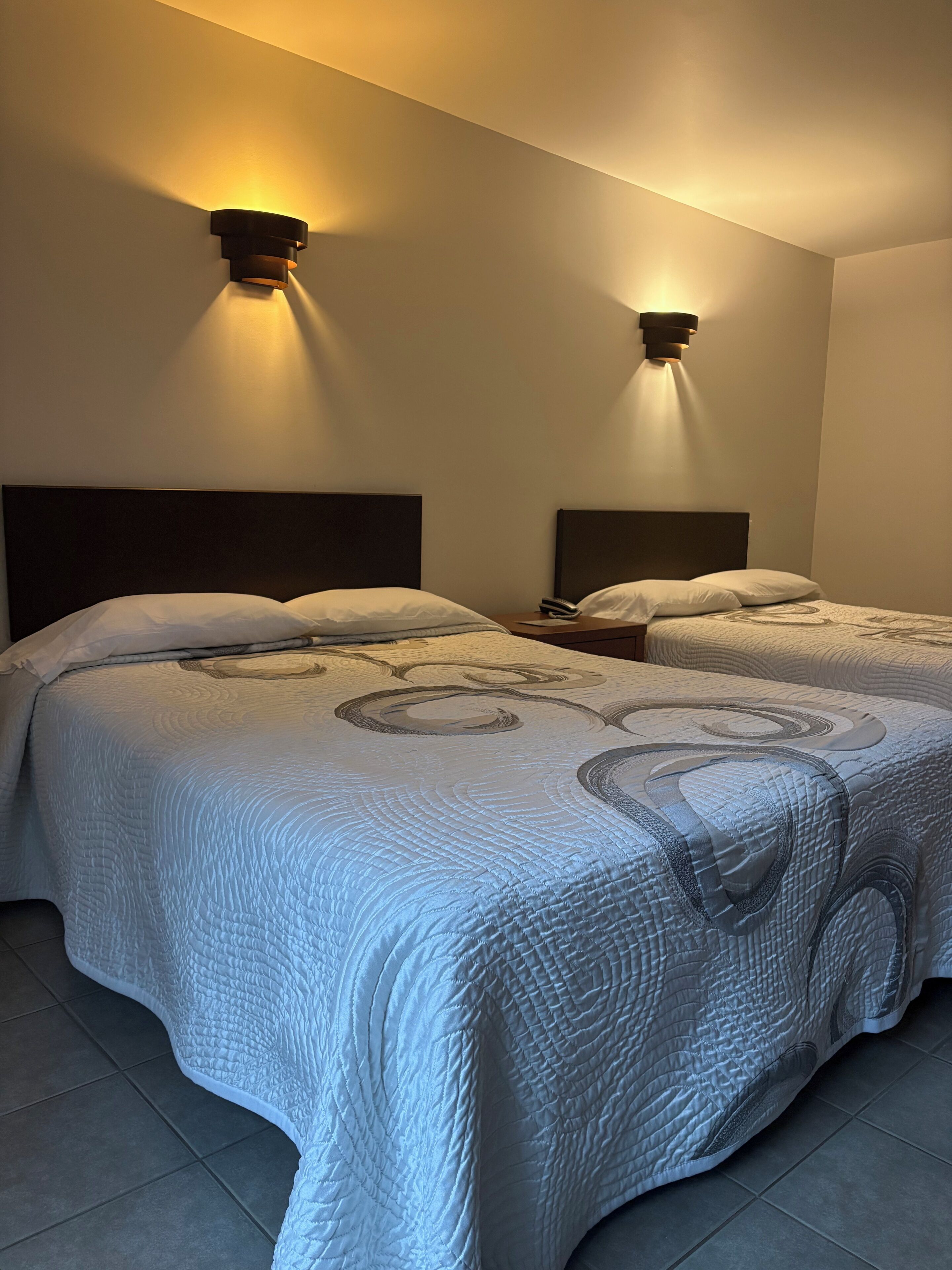 Quarto de hotel com duas camas, cada uma com cabeceira e mesa de cabeceira.