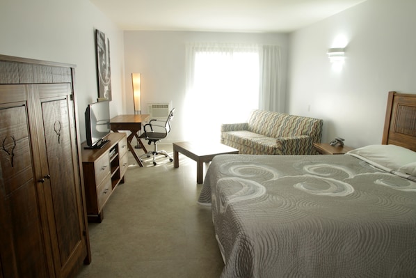 A hotel room with a bed, a desk with a chair, a wardrobe, and a window with curtains. - Motel Le Martinet (La Pocatiere)