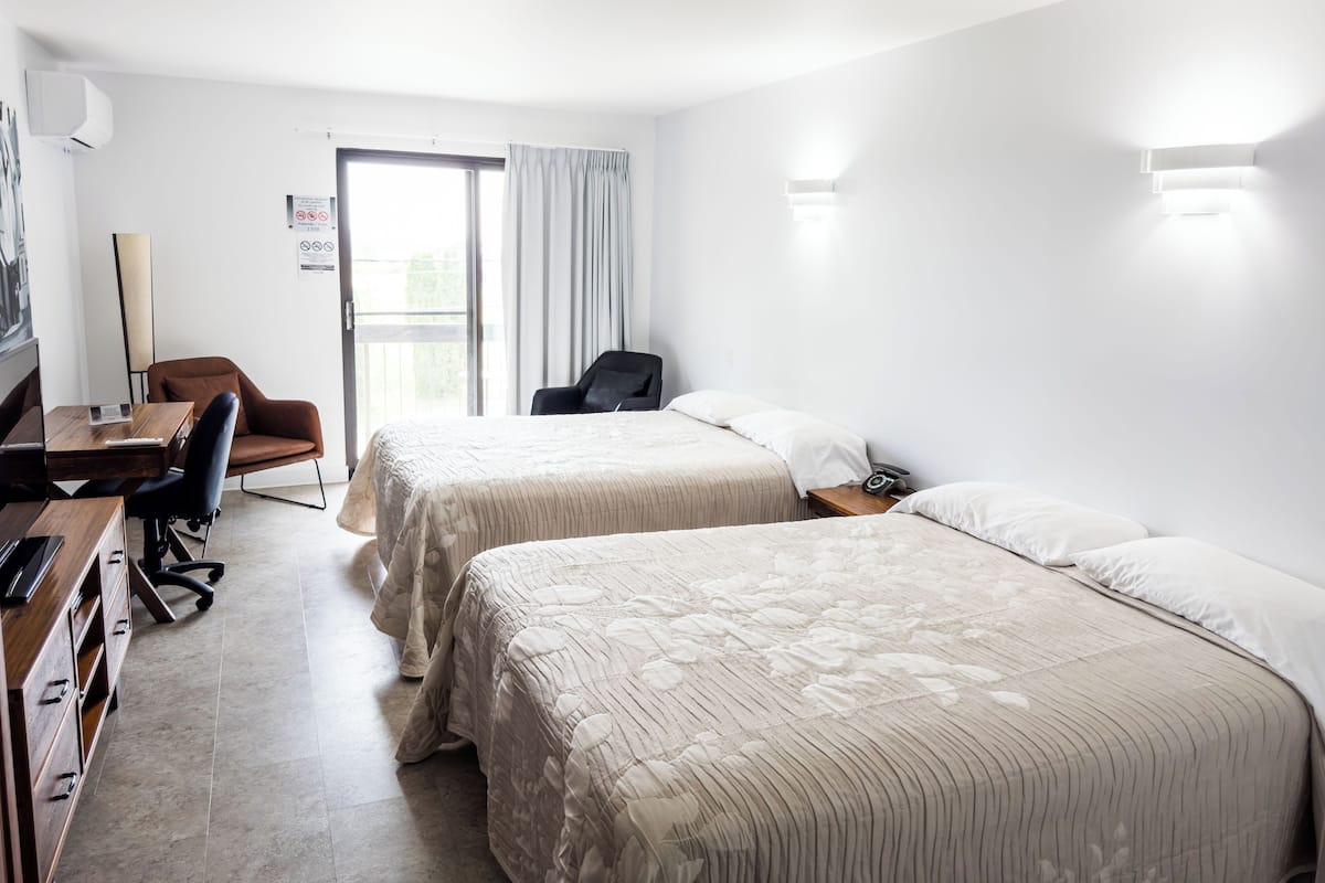 Une chambre d’hôtel avec deux lits, un bureau, une chaise et une grande fenêtre.
