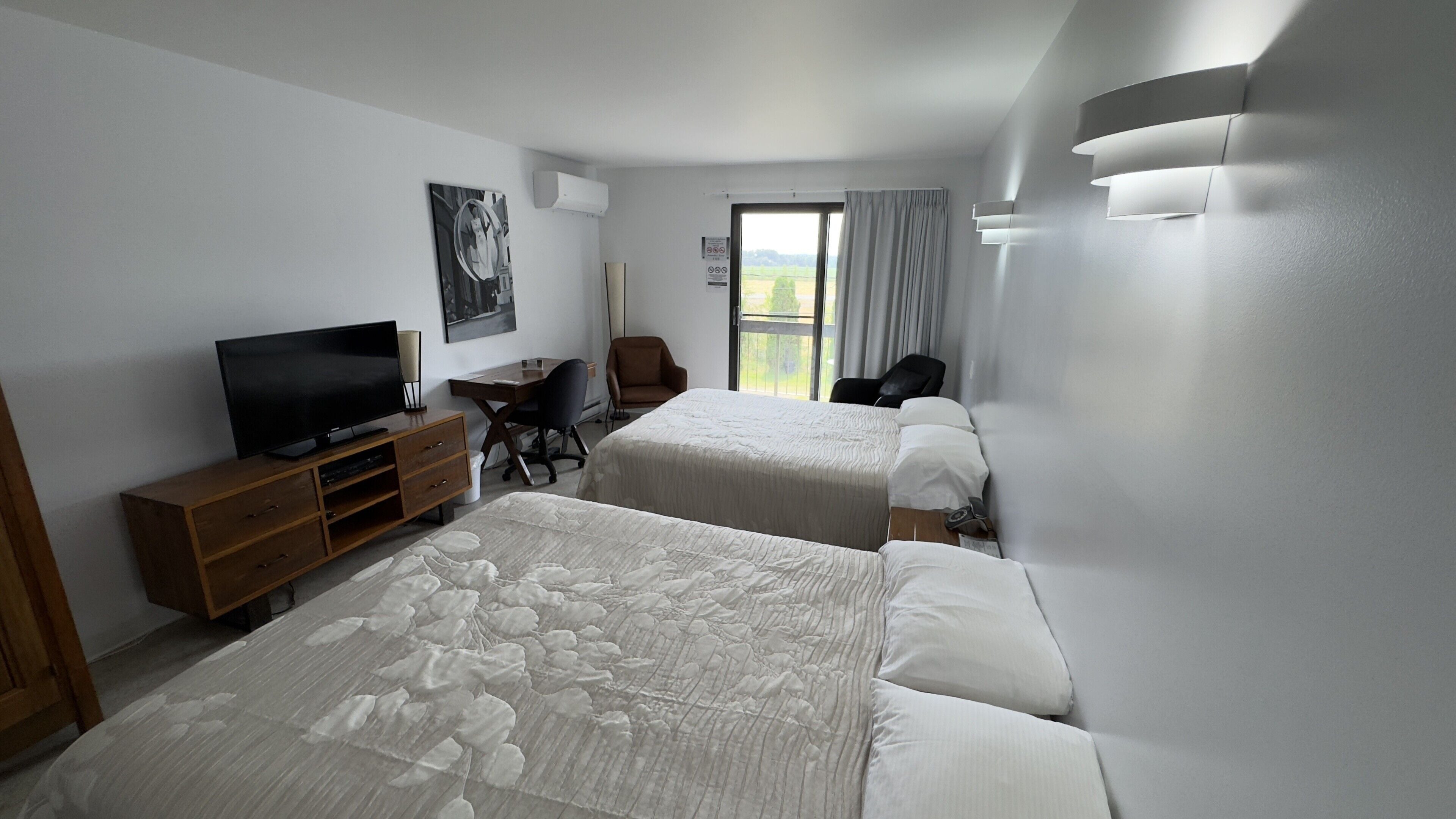 A hotel room with two beds, a desk, a chair, a television, and a window with curtains.