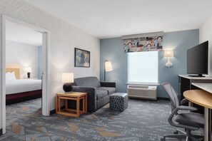 A hotel room with a bed, a sofa, a desk, a chair, a lamp, a television, and a window with a view.