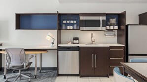 Cocina compacta equipada con microondas, lavavajillas y una pequeña zona de comedor con una silla y escritorio.