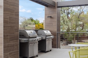 An outdoor patio with two stainless steel barbecue grills, a small round table, and yellow chairs. - Home2 Suites by Hilton Salt Lake City East (Salt Lake City)
