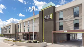 A modern hotel building with a sign reading 'HOME 2 Suites by Hilton' and a flagpole with an American flag.