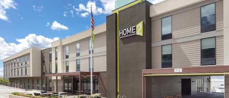 Un bâtiment moderne abritant un hôtel, avec une enseigne indiquant « HOME 2 Suites by Hilton » et un mât sur lequel flotte un drapeau américain.
