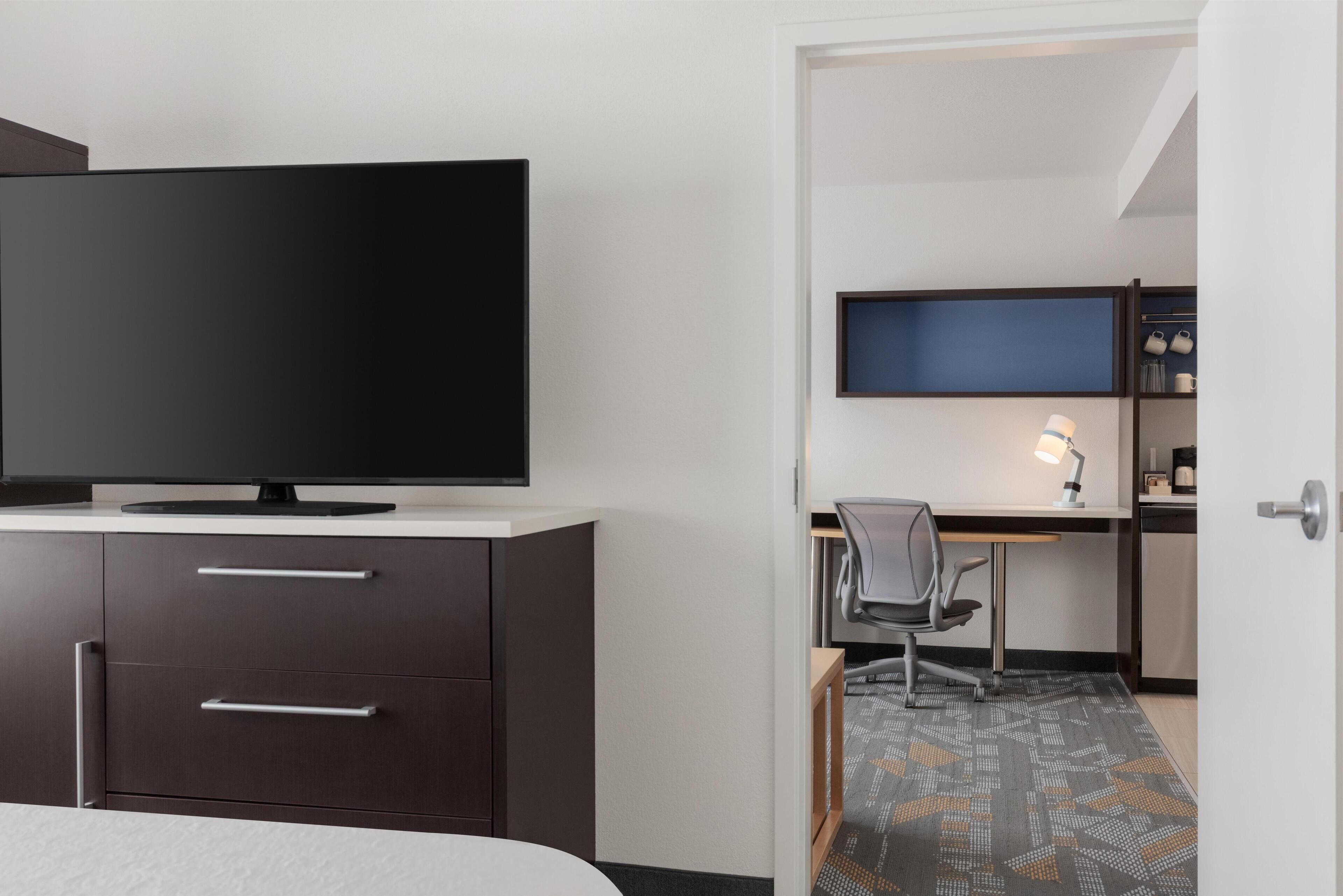 Habitación de hotel con cama, televisor, escritorio con silla y armario.