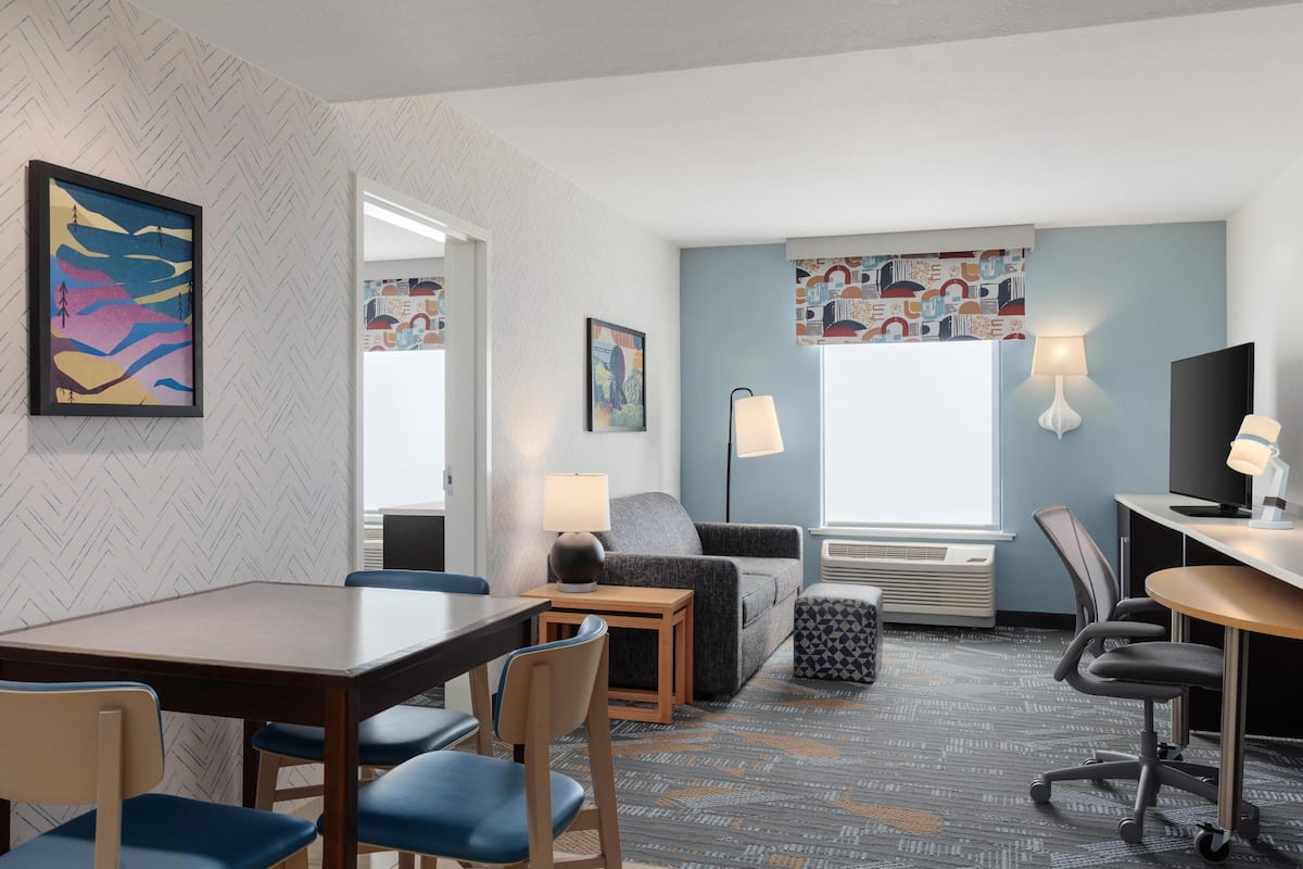 Ein Hotelzimmer mit Essbereich, einer Couch, einem Fernseher und Kunstwerken an den Wänden.