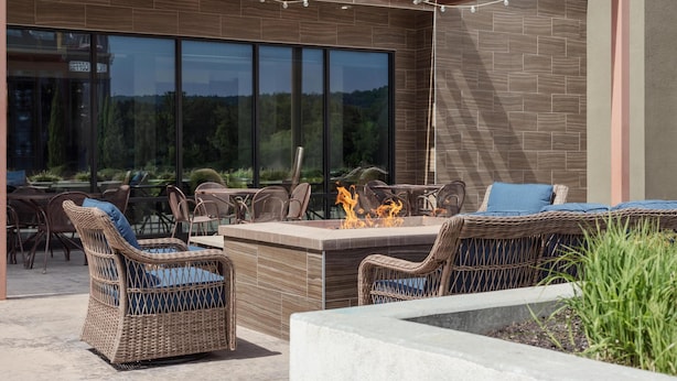 Un patio exterior con mobiliario de mimbre, una chimenea y vistas al bosque a través de amplios ventanales.