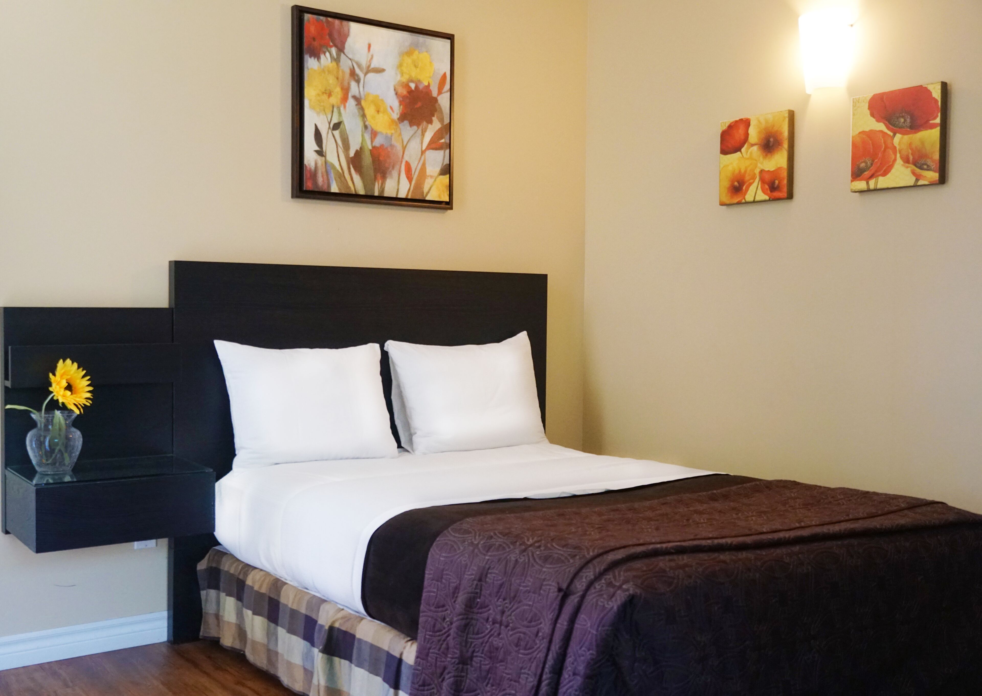 Una habitación de hotel con una cama, una mesita de noche con un jarrón de flores y tres cuadros colgados en la pared.
