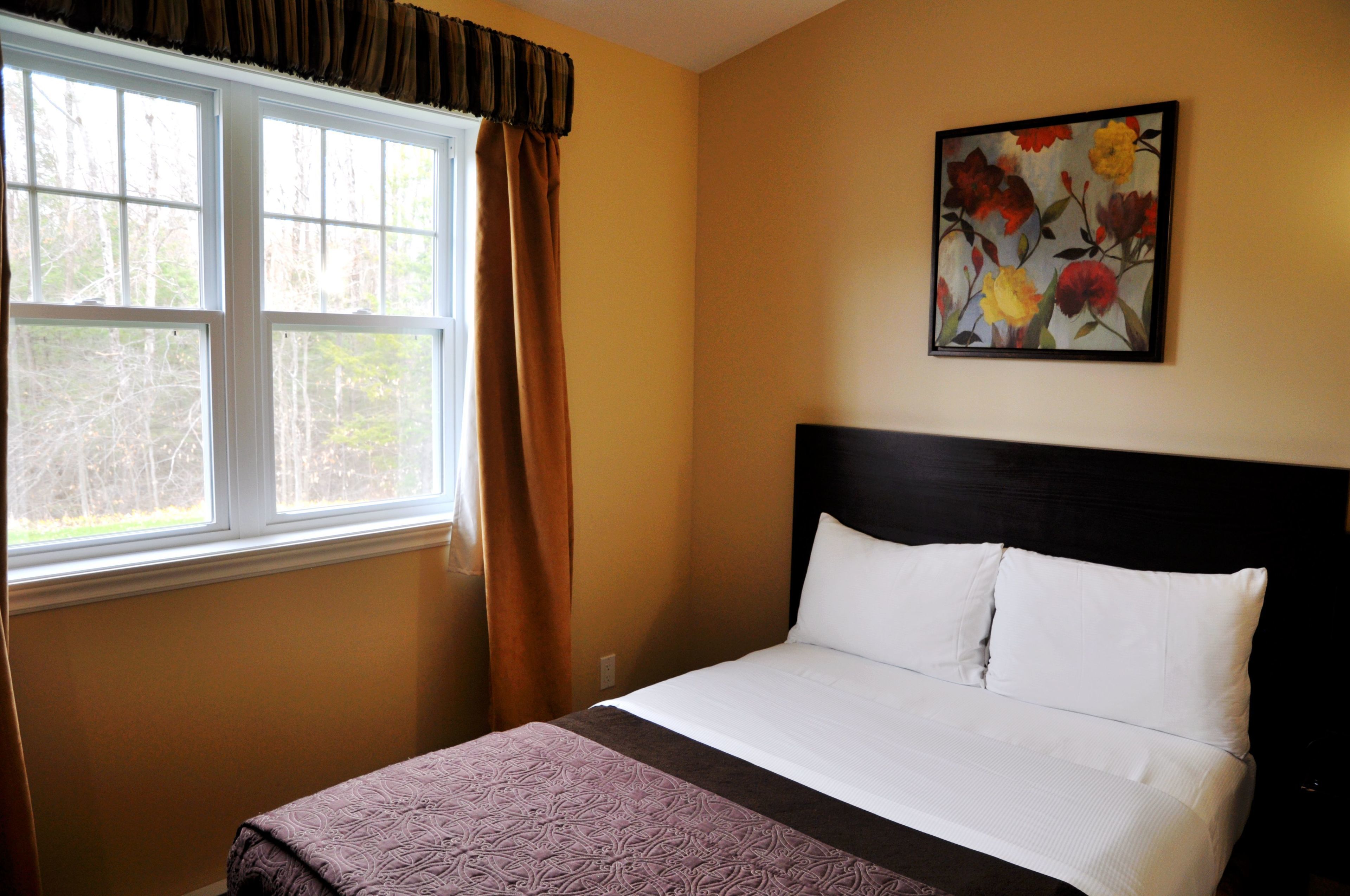 A bedroom with a bed, a window with curtains, and a floral painting on the wall.