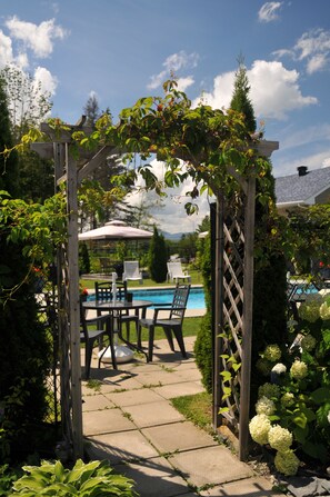 A wooden pergola with climbing plants, a pool, and outdoor furniture. - Motel des Cèdres (Sherbrooke)