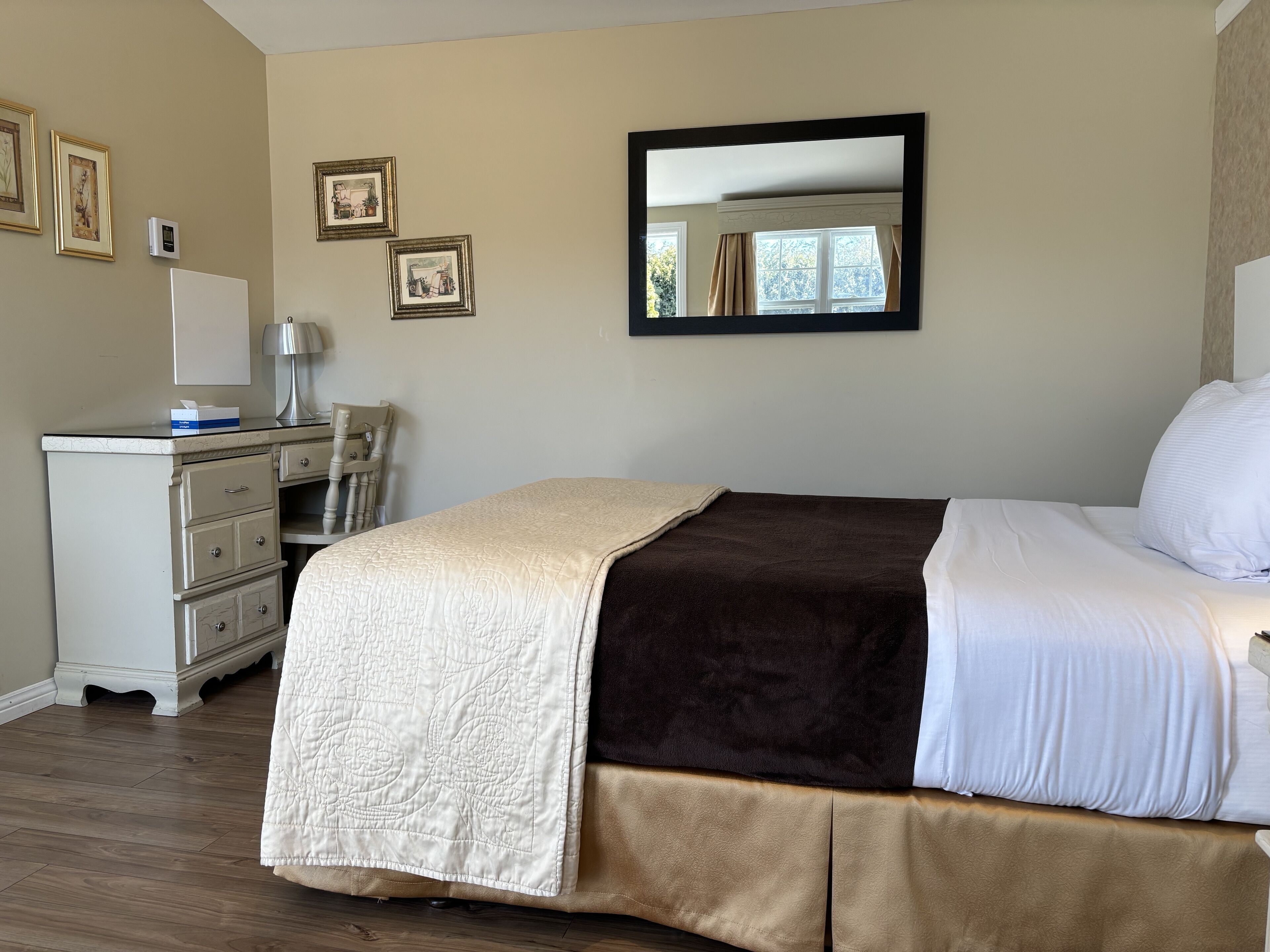 A neatly arranged bedroom with a bed, a dresser, a desk, and a mirror on the wall.