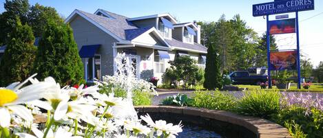 A motel with a signboard, a small water feature, and a garden with flowers.