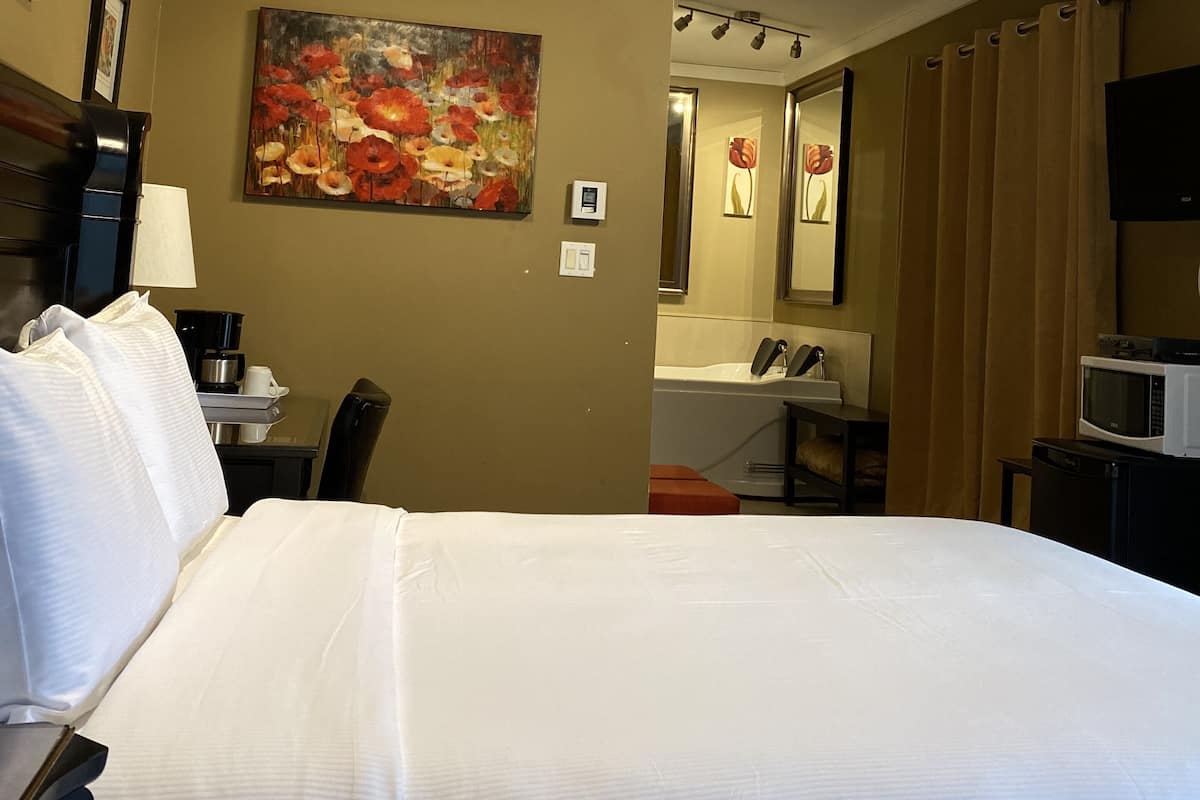 A hotel room with a large bed, a painting on the wall, a desk with a lamp, a coffee maker, and a microwave on a small table.