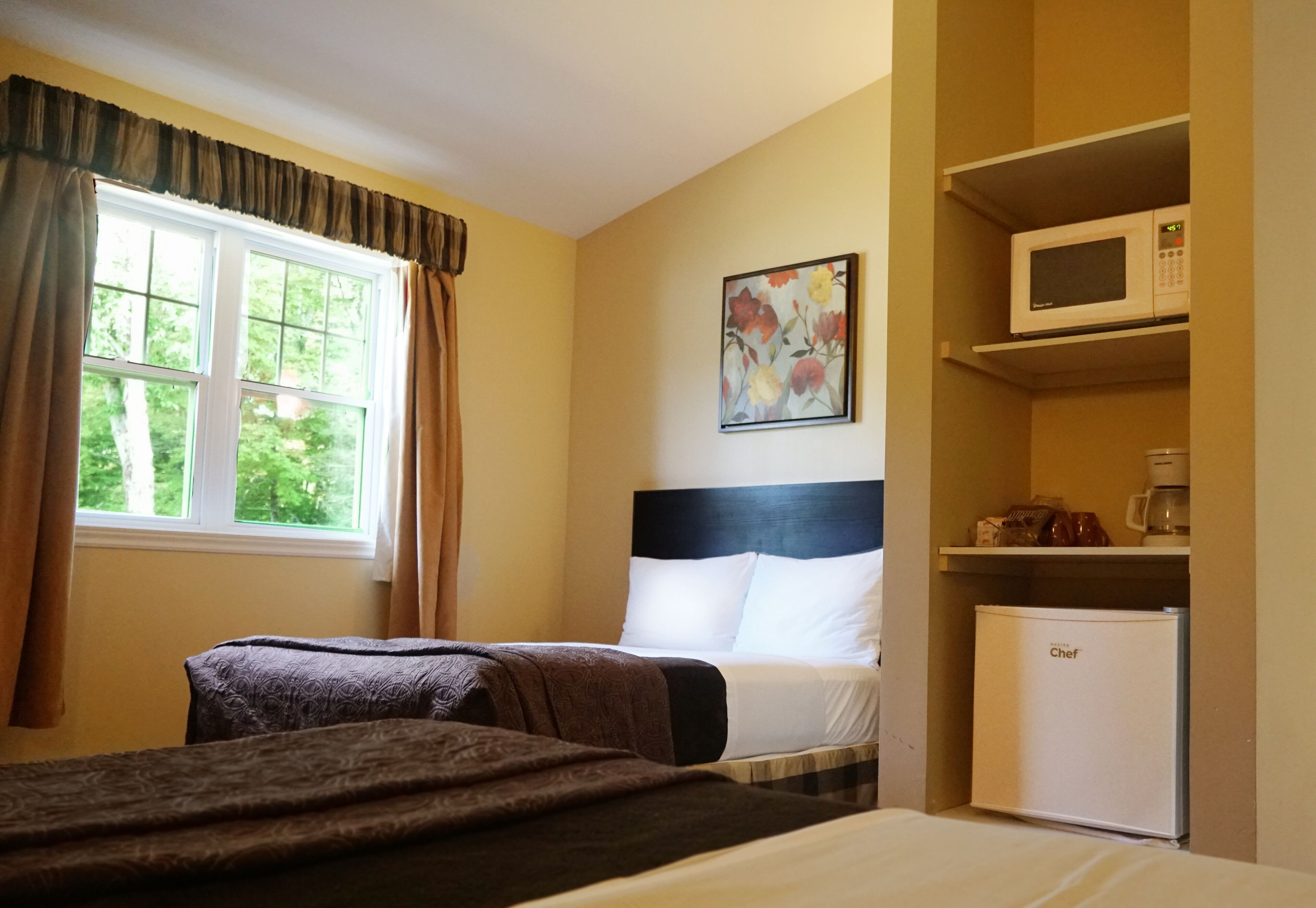 Una camera d'albergo con un letto, una finestra con tende, un forno a microonde e un frigorifero.