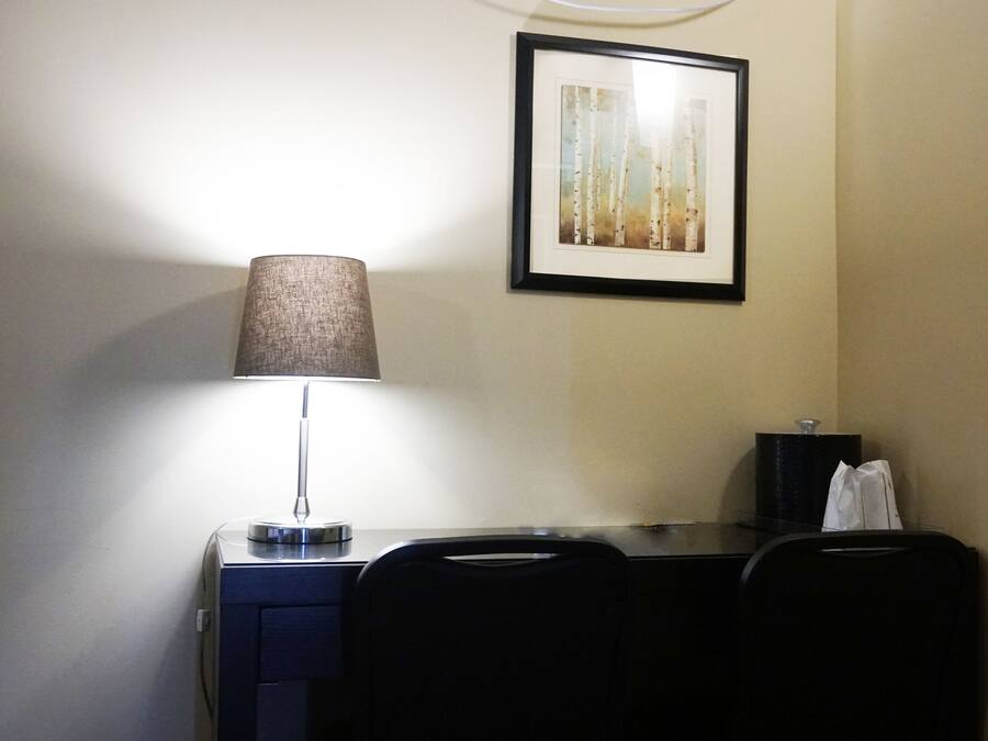 A desk with a lamp, a framed picture on the wall, and a black bag on the desk.
