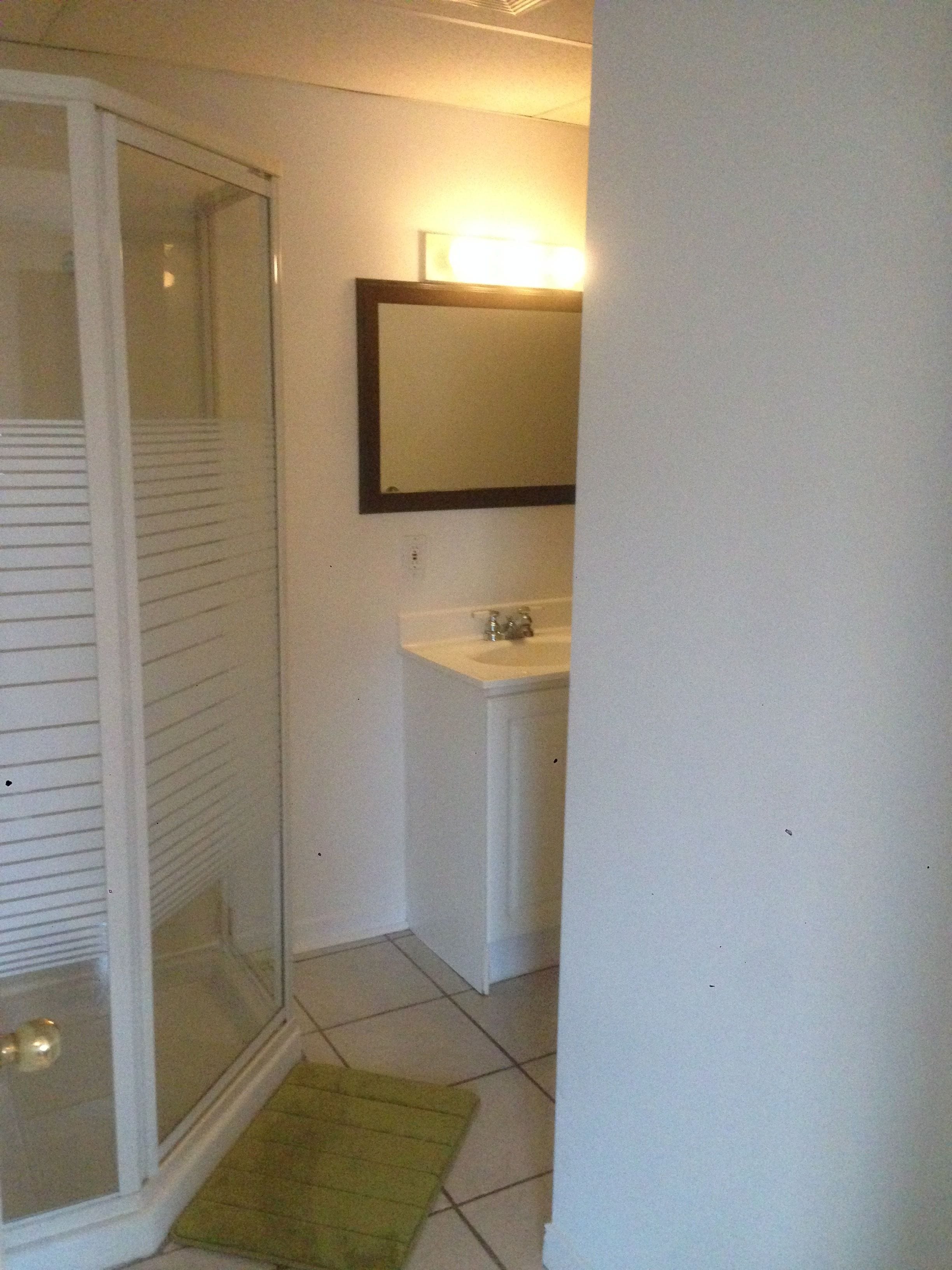 Un baño con mampara de vidrio, lavamanos blanco y espejo superior.