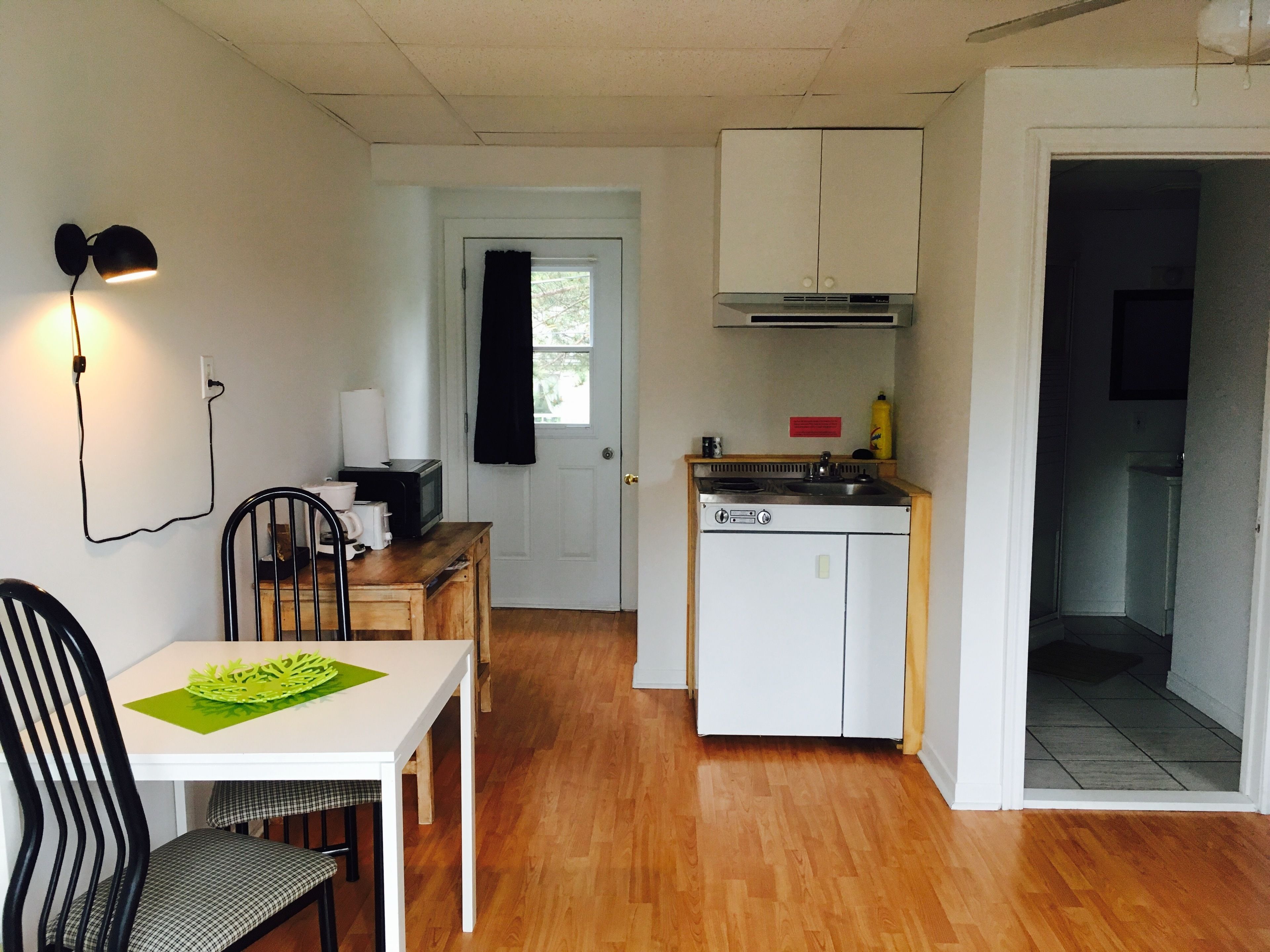 A compact kitchen with a stove, sink, and cabinets. There is a dining table with chairs and a lamp on the wall.
