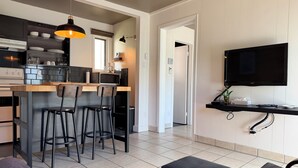 A modern kitchen with a central island, bar stools, a dining table, and a TV mounted on the wall. - Attitude Montagne (St-Adolphe-d'Howard)