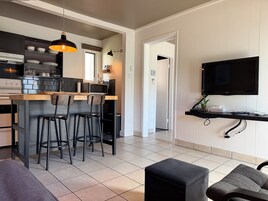 Una cocina moderna con una isla central, taburetes de bar, una mesa de comedor y un televisor montado en la pared.