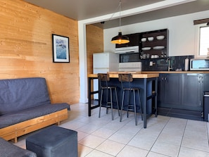 A modern kitchen with a wooden wall, a dining area with stools, a sofa, and a refrigerator. - Attitude Montagne (St-Adolphe-d'Howard)