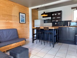 Una cocina moderna con pared de madera, una zona de comedor con taburetes, un sofá y un refrigerador.