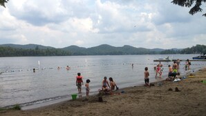 A beach with people playing and swimming, boats in the water, and hills in the background. - Attitude Montagne (St-Adolphe-d'Howard)