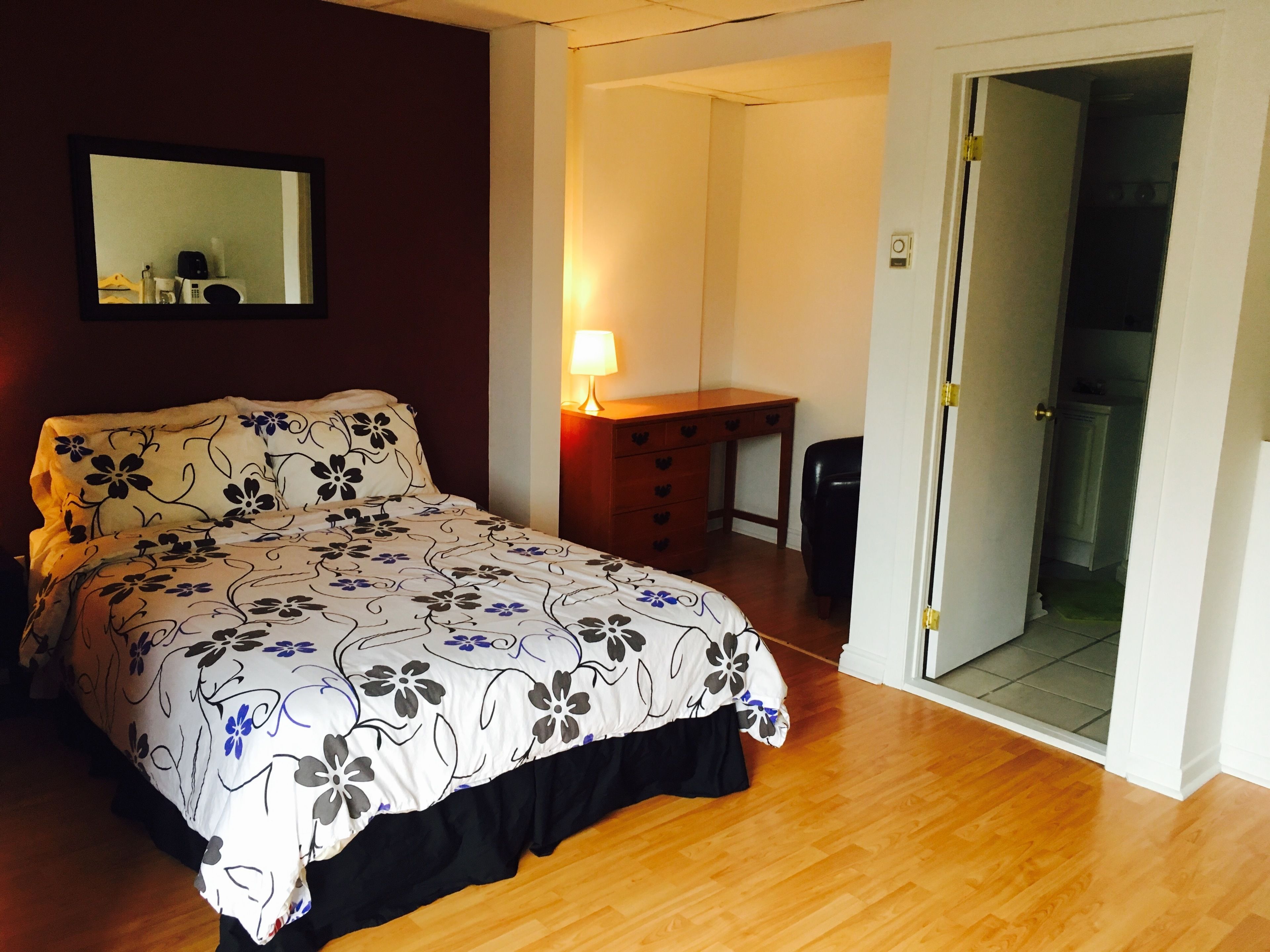 A bedroom with a bed, a desk, a lamp, and a door leading to a bathroom.