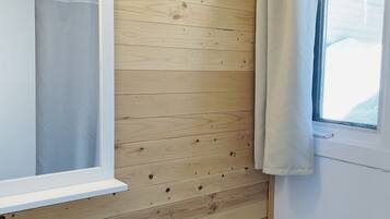 A bathroom with wooden panel walls, a white sink with glass soap dispensers, a toilet, and a window with a curtain.