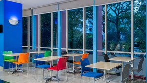 Un espacio interior moderno con ventanas amplias, varias mesas y sillas coloridas.