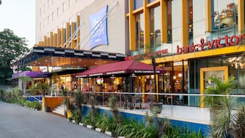 Un hotel con una fachada moderna, varias opciones de restauración y un área exterior ajardinada.