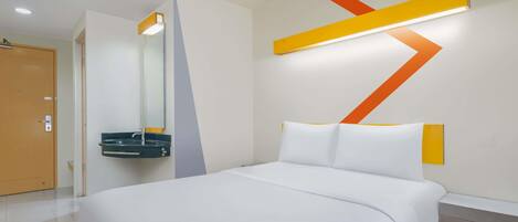 A modern hotel room with a large bed, a bedside table, a mirror, and a wall-mounted light fixture.