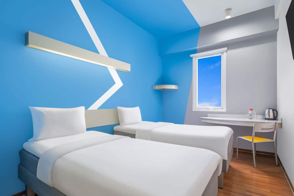 A hotel room with two beds, a desk, a window, and a modern design.